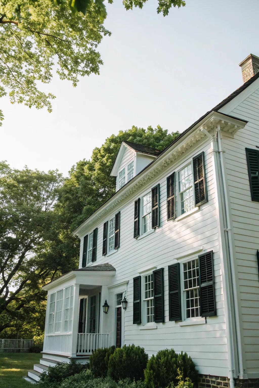 A quintessential colonial dwelling showcasing a white facade contrasted by dark window coverings.
