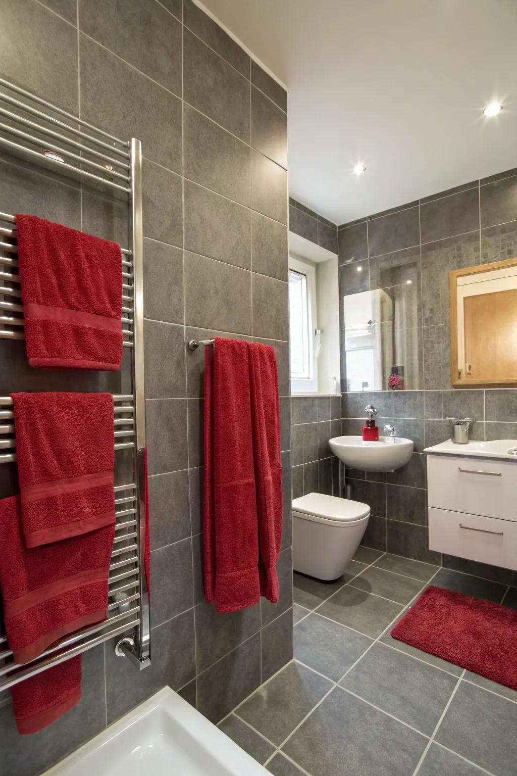 A bath space showcases grey tiling and scarlet accessories.